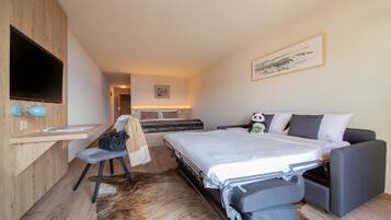 Habitación de hotel con cama, escritorio, silla, televisor y un peluche de panda.