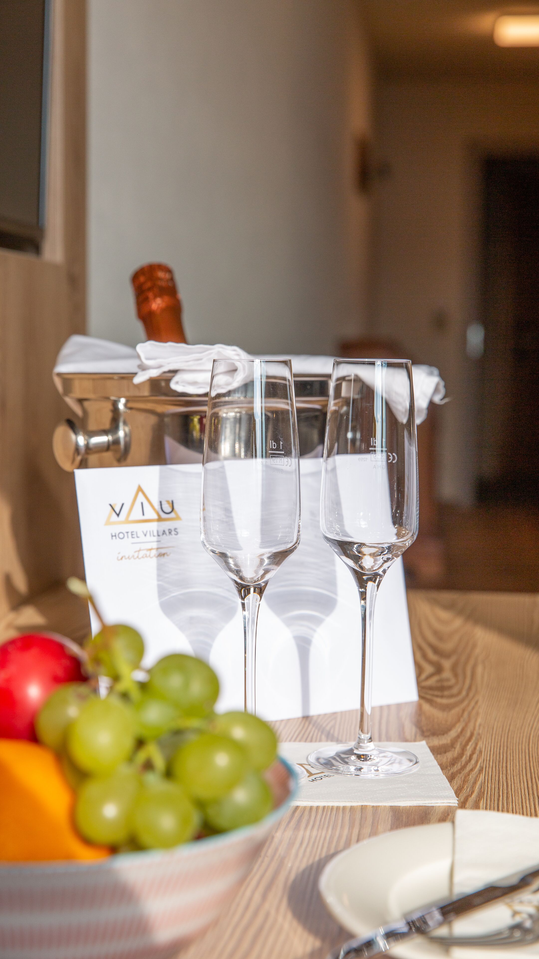 Una mesa con una botella de champán, tres copas, un plato de uvas y una servilleta.