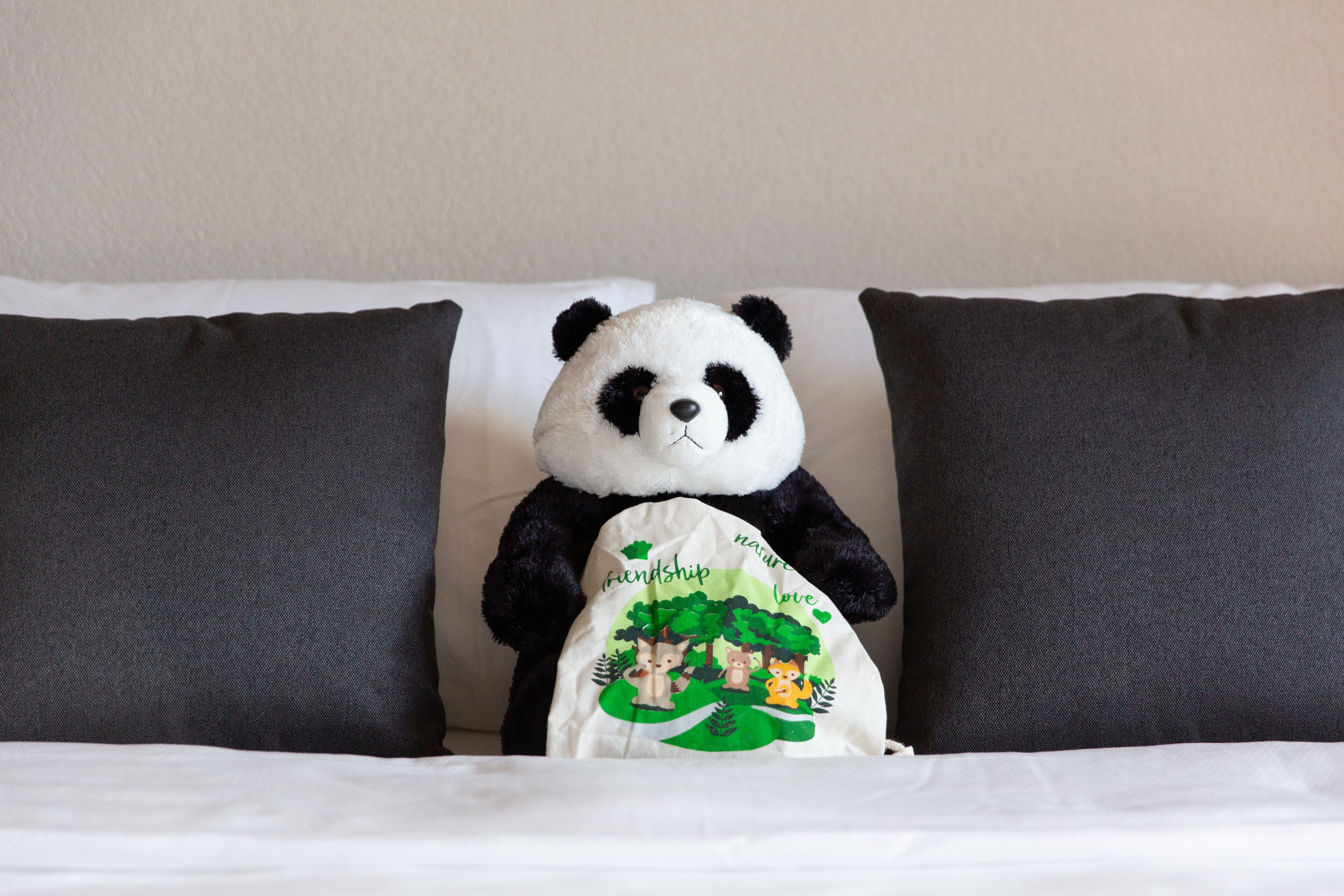 A plush panda toy on a bed with white and dark gray pillows.