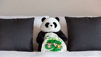 A plush panda toy on a bed with white and dark gray pillows.