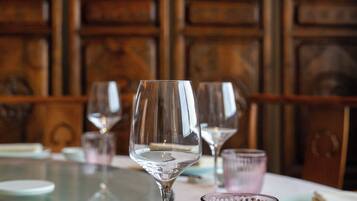 A table with wine glasses and a glass bowl, set against a wooden wall with intricate carvings.