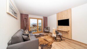 Uma sala de estar moderna com um sofá cinzento, um móvel para TV de madeira e uma janela grande com vista para montanhas.