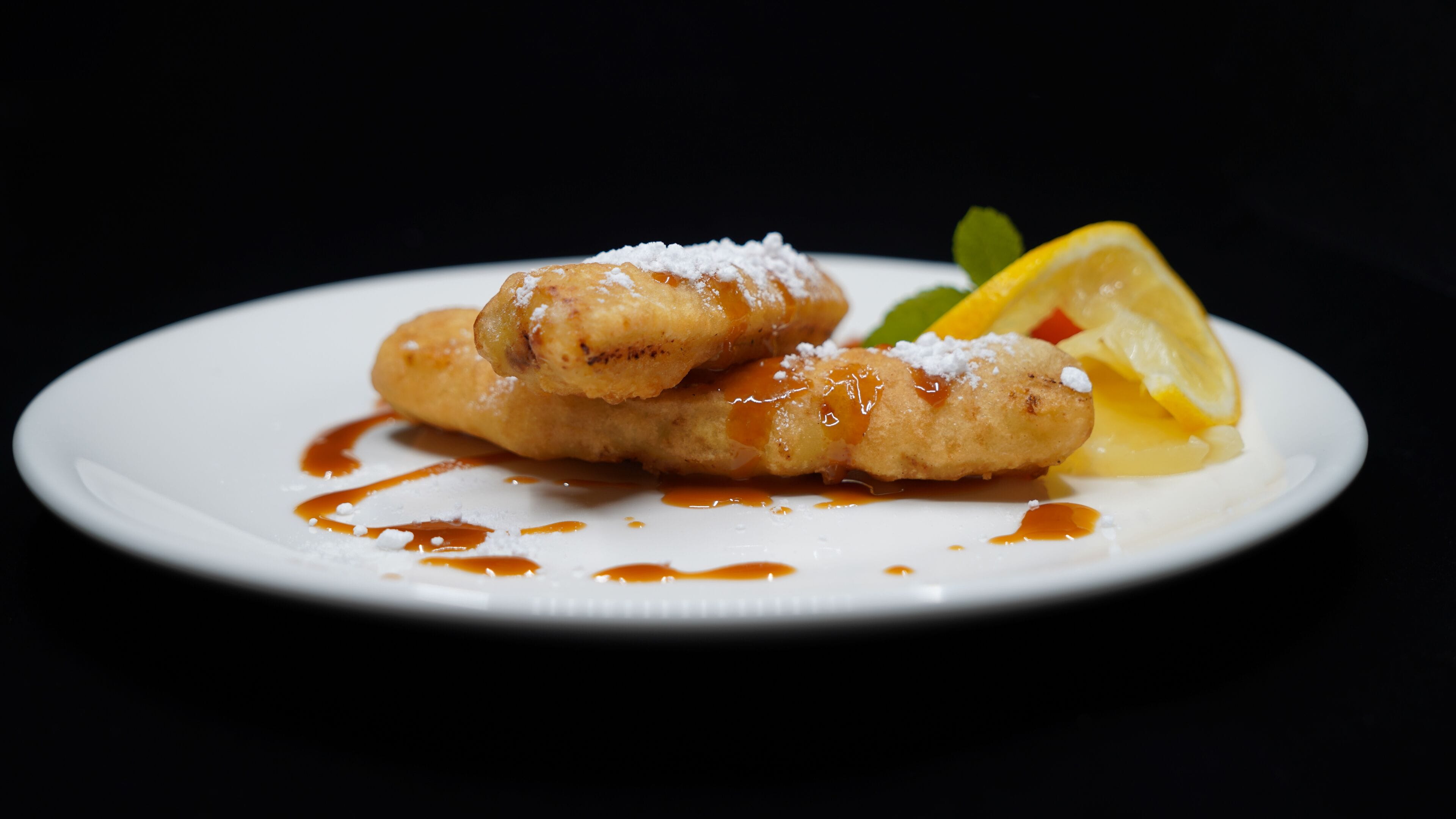 A plate with two fried pastries, a lemon slice, and a mint leaf.