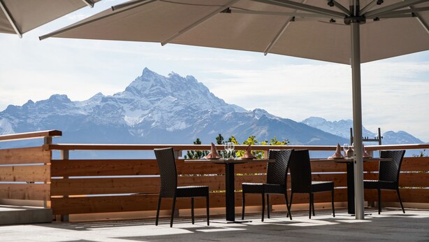 A terrace with wooden railings, a table with chairs, and a view of snow-capped mountains. - VIU Hotel Villars (Ollon)