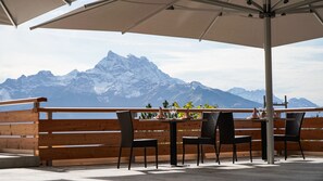 Una terraza con barandillas de madera, una mesa con sillas y vistas a montañas nevadas.