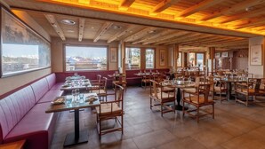 A restaurant with wooden beams, large windows, and a mix of booths and tables. - VIU Hotel Villars (Ollon)