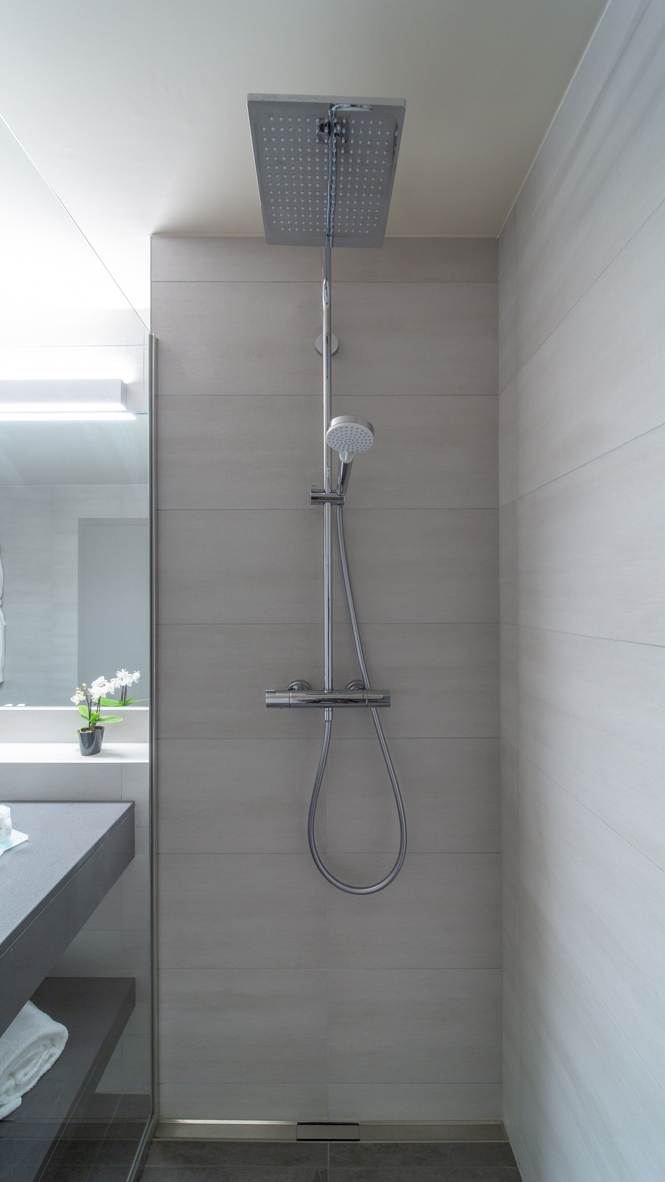 Une douche moderne dotée d’un pommeau de douche à main et d’un grand pommeau de douche suspendu imitant une pluie.