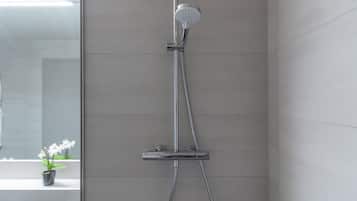 Une douche moderne dotée d’un pommeau de douche à main et d’un grand pommeau de douche suspendu imitant une pluie.