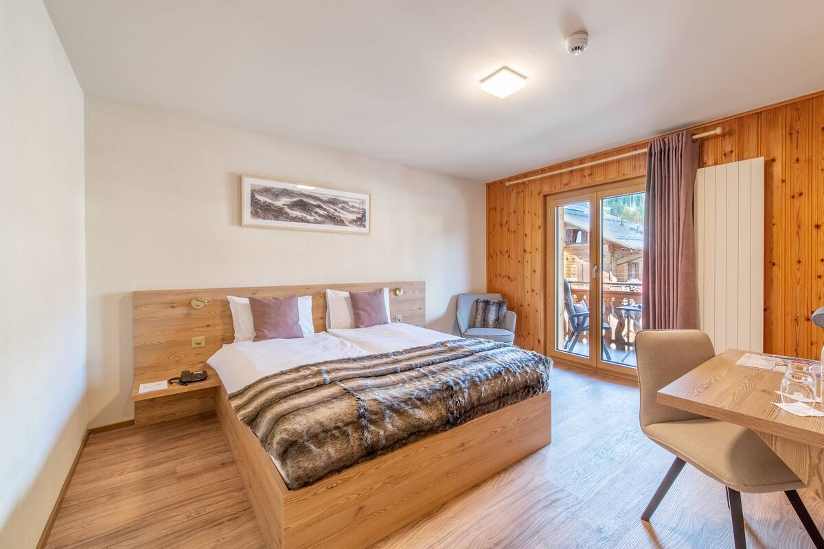 Un dormitorio con cama de madera, un escritorio y una silla. Hay una ventana con cortinas, un cuadro en la pared y una lámpara en el techo.