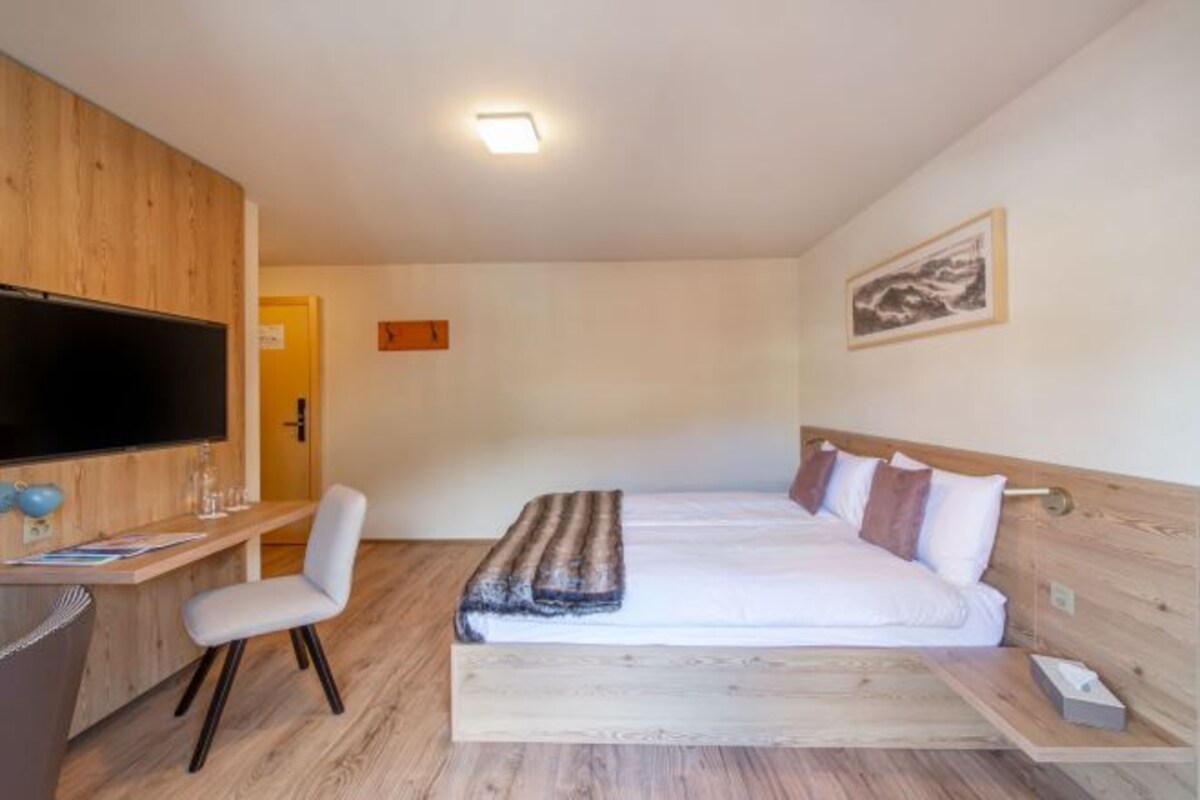 A hotel room with a bed, a desk with a chair, a television, and a framed picture on the wall.