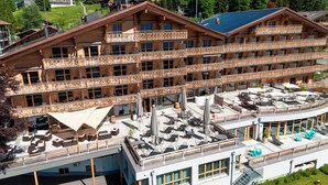 A multi-story wooden hotel with balconies, outdoor seating, and a pool area. - VIU Hotel Villars (Ollon)