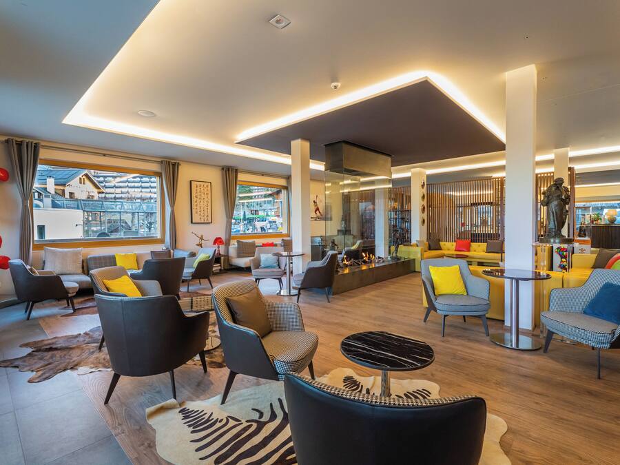 Un moderno vestíbulo de hotel con diversas zonas de estar, una chimenea y grandes ventanales que ofrecen vistas de la ciudad.