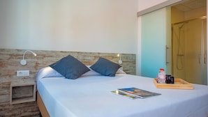 Una cama bien hecha con almohadas, una mesita de noche con una revista, una botella y una bandeja con artículos de aseo.