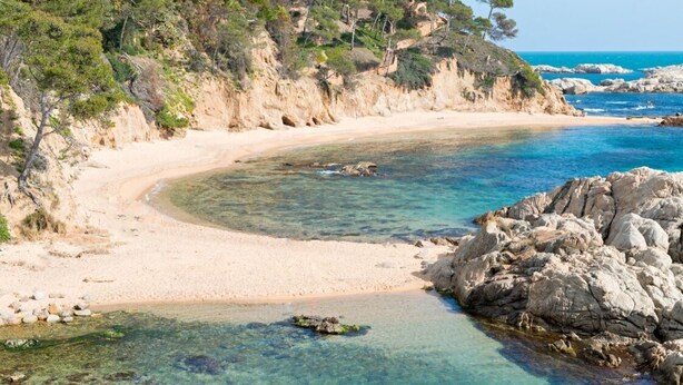 Una playa costera con aguas cristalinas, orillas de arena y afloramientos rocosos.
