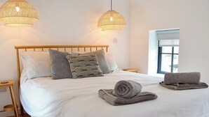 A neatly made bed with a white comforter, two patterned pillows, and a rolled towel on a wooden headboard. - The Hen House-UK12928 (Nancherrow, near Penzance)