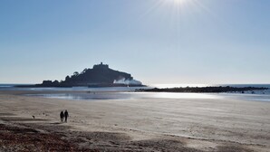 A beach with a castle-like structure in the background, a clear sky, and the sun shining brightly. - The Hen House-UK12928 (Nancherrow, near Penzance)