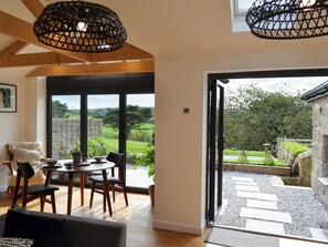 A dining area with a table and chairs, a sofa, and a view of the outdoors through large windows. - The Hen House-UK12928 (Nancherrow, near Penzance)