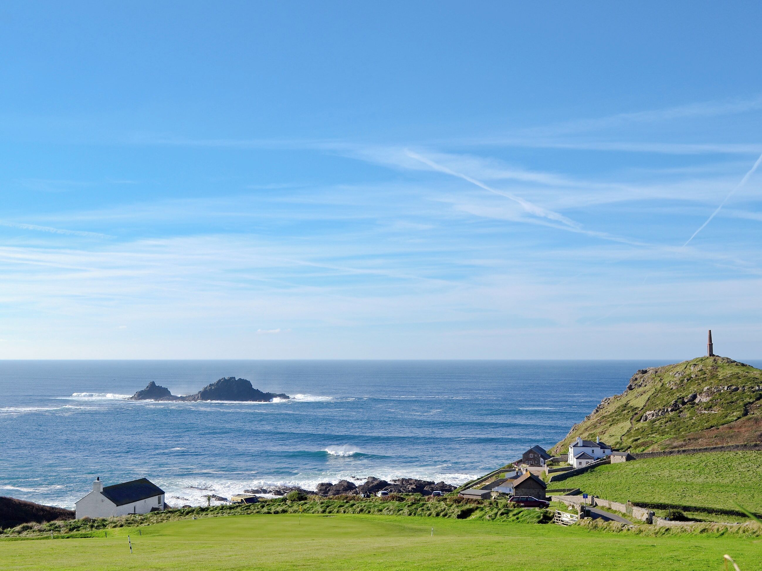 A coastal landscape with a grassy area, a small white building, and a stone structure on a hill.