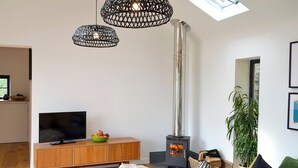 A modern living room with a large TV, a wooden cabinet, a green bowl of fruit, a fireplace, and a skylight. - The Hen House-UK12928 (Nancherrow, near Penzance)