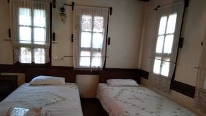 A room with two single beds, each with a white bedspread and a pillow. There are windows with curtains, a wall-mounted lamp, and a wooden headboard. - Safranbolu Konagi (Safranbolu)