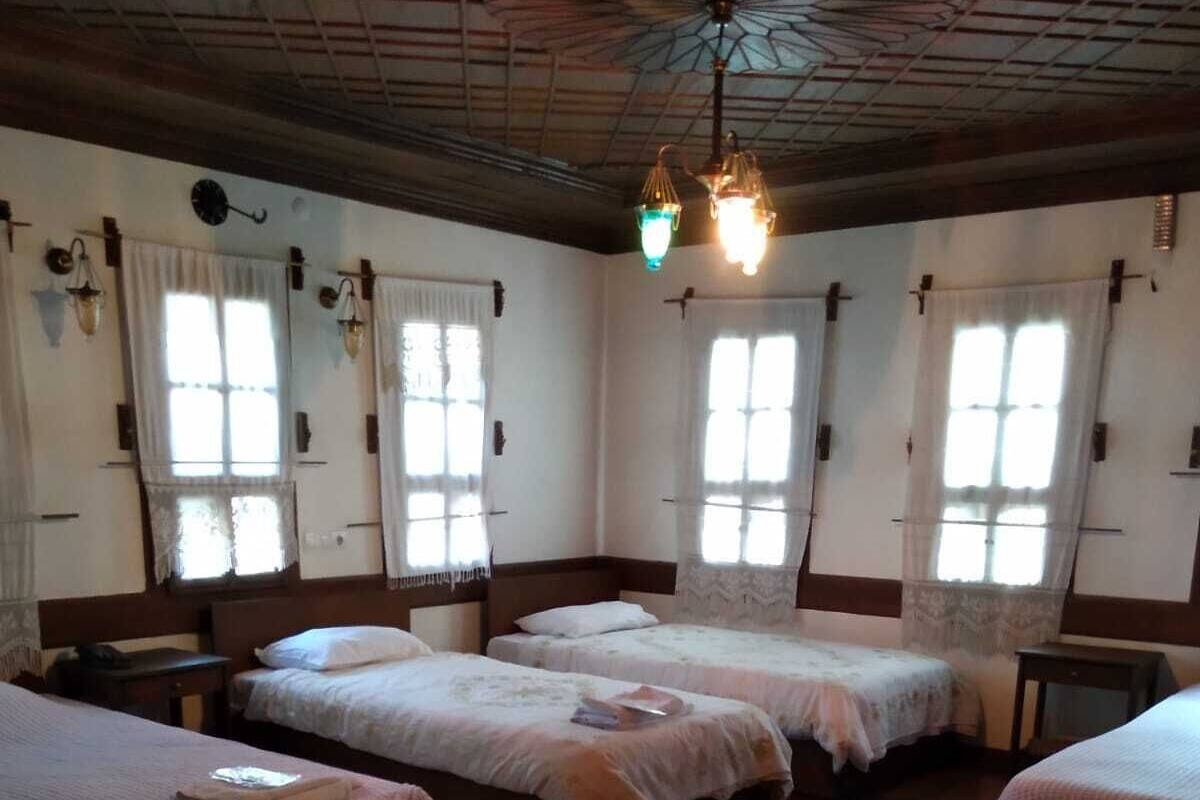 A room with four beds arranged in a row, wooden beams on the ceiling, and a patterned rug on the floor.