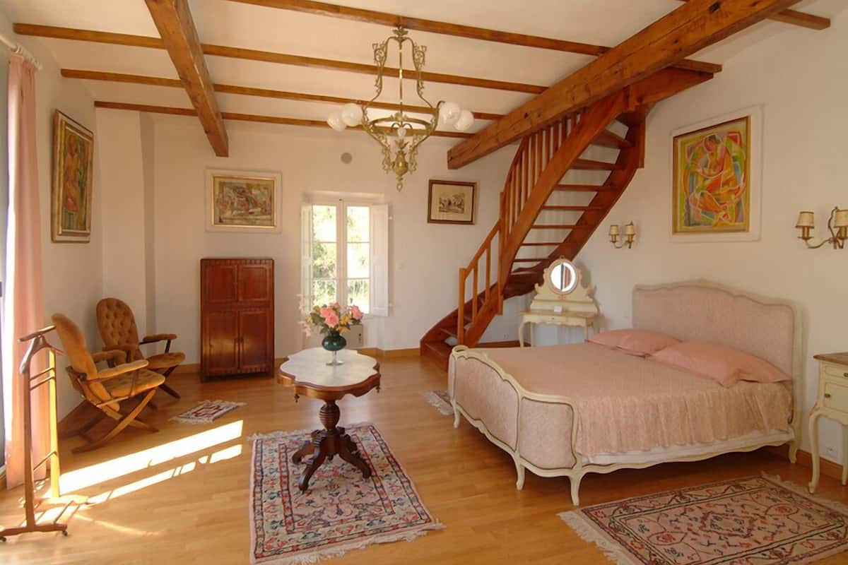 Une chambre avec un escalier en bois, un lit, une chaise, une table et un lustre.