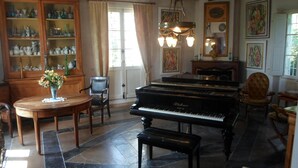 Un vaste salon agrémenté d’un magnifique piano à queue, d’un meuble en bois aux portes vitrées, d’une cheminée et d’une grande fenêtre ornée de rideaux.