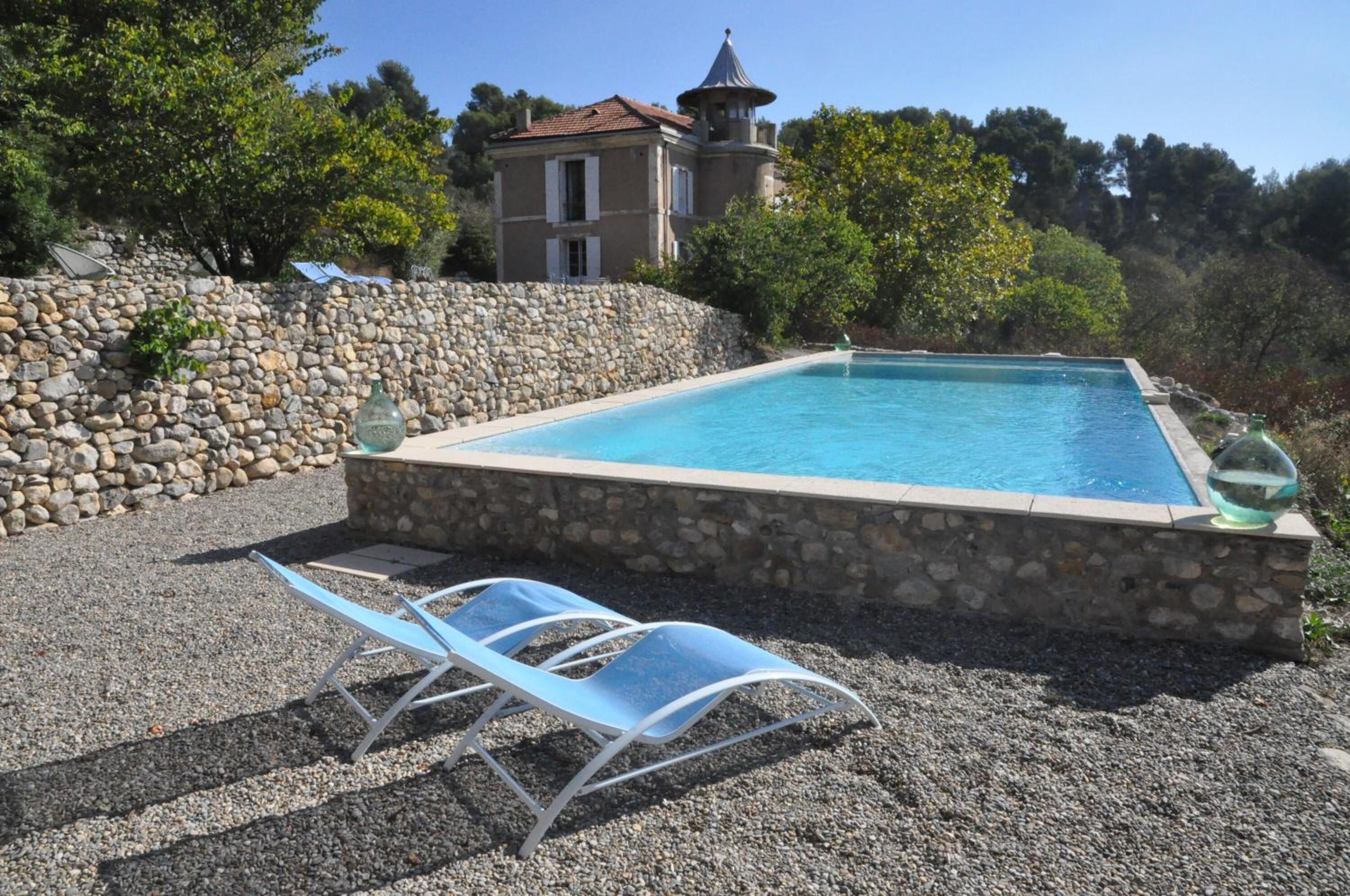 Una piscina con paredes y sendero de piedra, rodeada de árboles y un edificio con torreón.