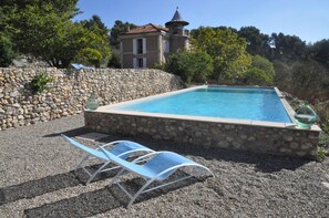 Una piscina con paredes y sendero de piedra, rodeada de árboles y un edificio con torreón.