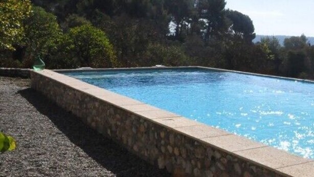 Une piscine rectangulaire bordée de pierres, entourée de verdure et offrant une vue sur des collines lointaines.