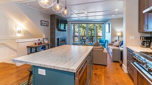 A modern kitchen with a marble countertop, stainless steel appliances, and pendant lighting.