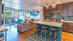 A modern kitchen with wooden cabinets, a central island with stools, and a large window overlooking a patio.