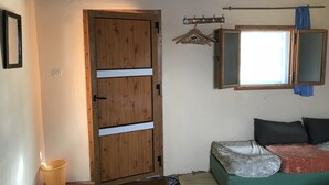 Una habitación con puerta de madera, ventana con vistas, cama con almohadas, una cesta pequeña y un perchero con ganchos.
