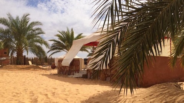 Una playa arenosa con palmeras y una estructura blanca de techo rojo.