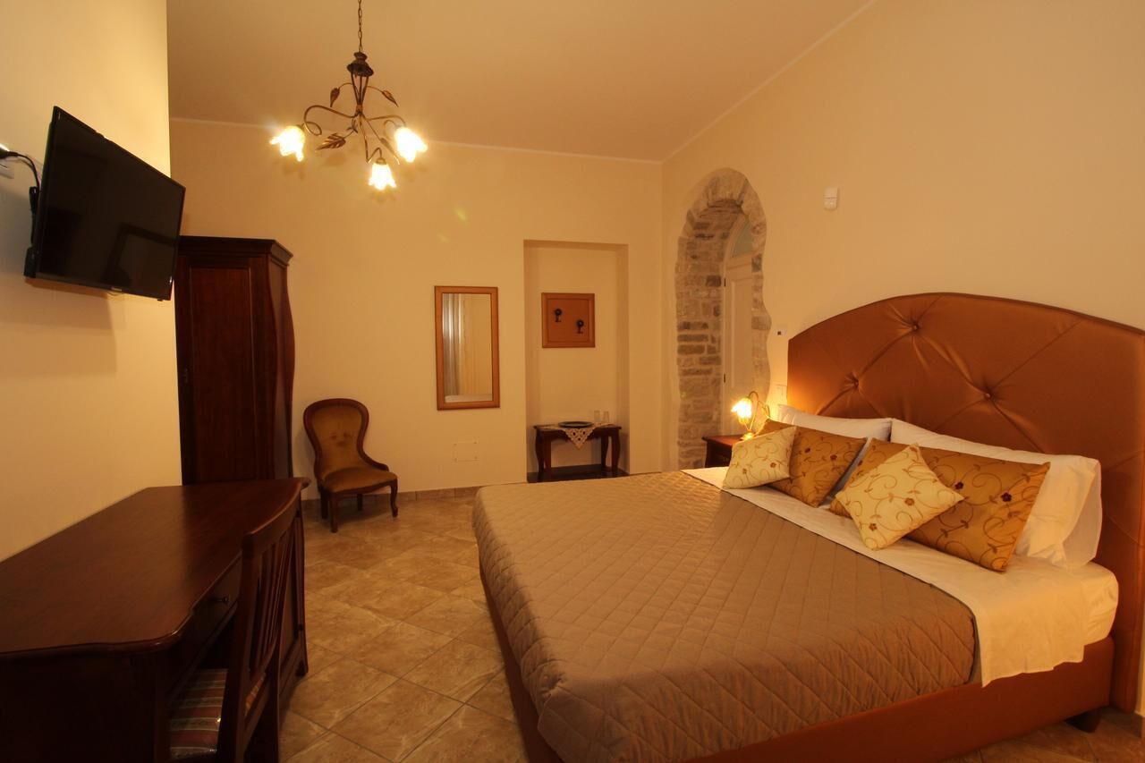 Een slaapkamer met een groot bed, een aan de muur bevestigde televisie, een houten bureau, een stoel en een kroonluchter.