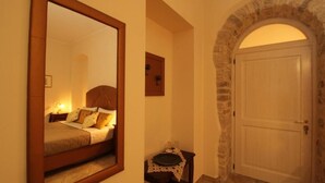 A bedroom with a bed, a bedside table, a mirror, and a door with a stone archway. - Palazzo 1892 (Castelvetere in Val Fortore)