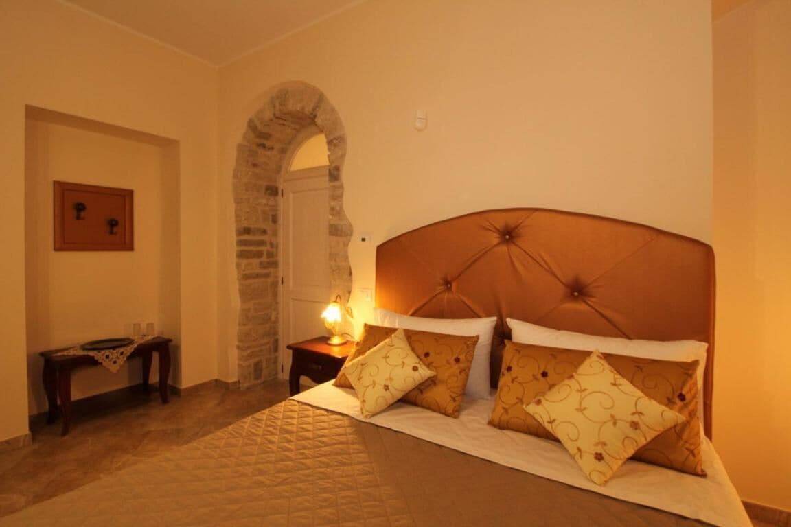 Un dormitorio con una cama grande, un arco de piedra, una mesita de noche con lámpara y un cuadro en la pared.