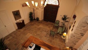 A spacious lobby with a high ceiling, a chandelier, a wooden reception desk, and a stone wall. - Palazzo 1892 (Castelvetere in Val Fortore)