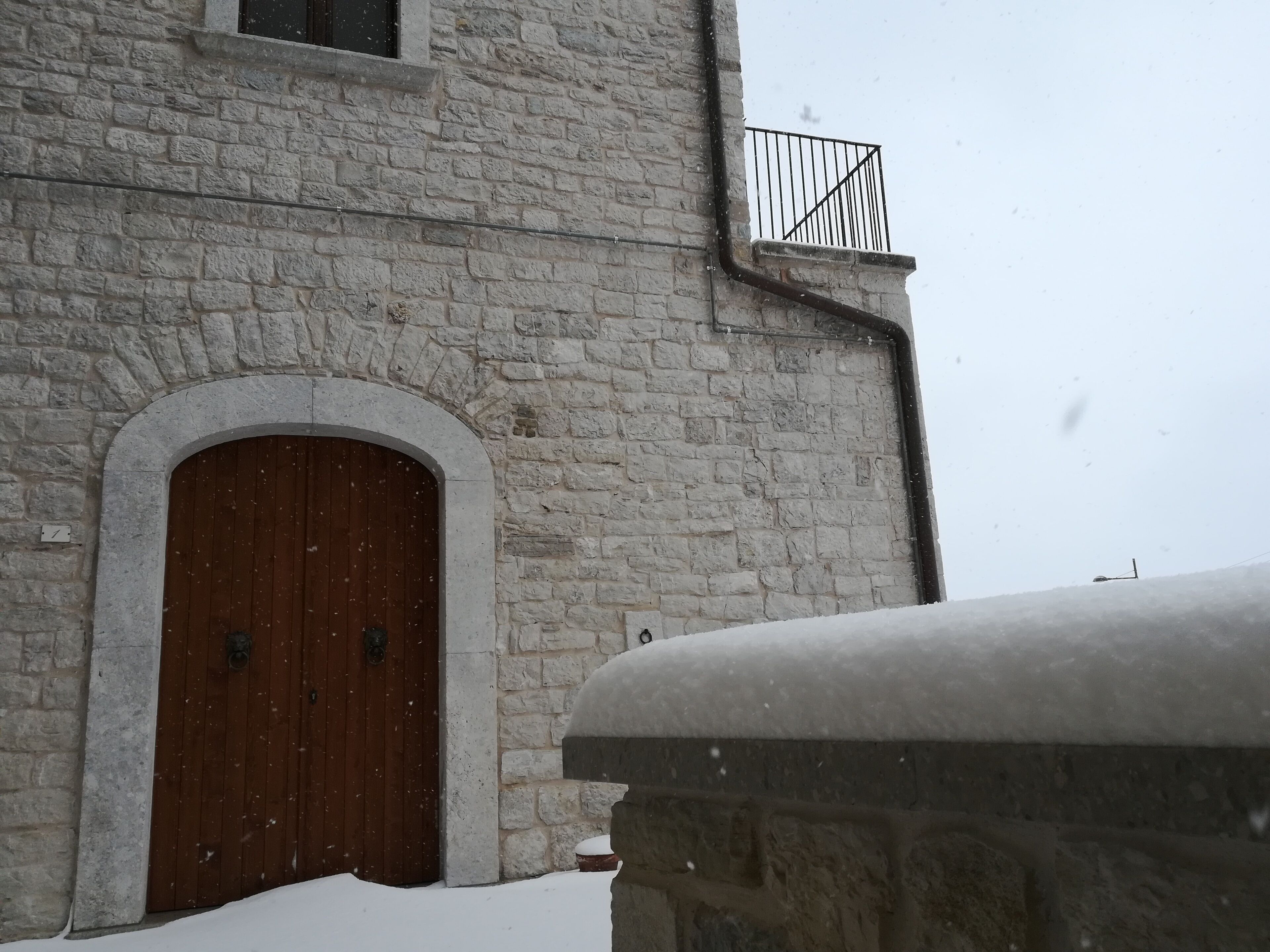 A stone building with a wooden door and a metal balcony railing.