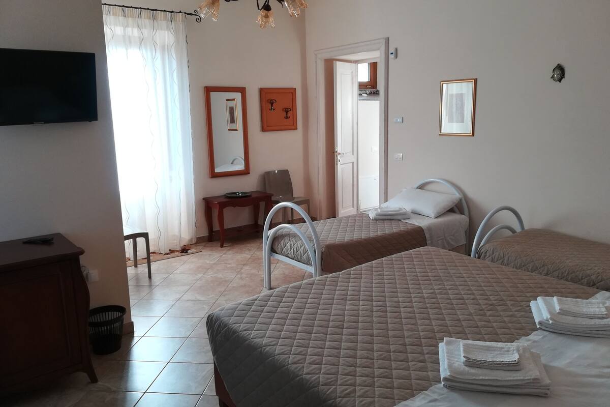 A hotel room with two beds, a desk, a chair, a television, and a door leading to a balcony.