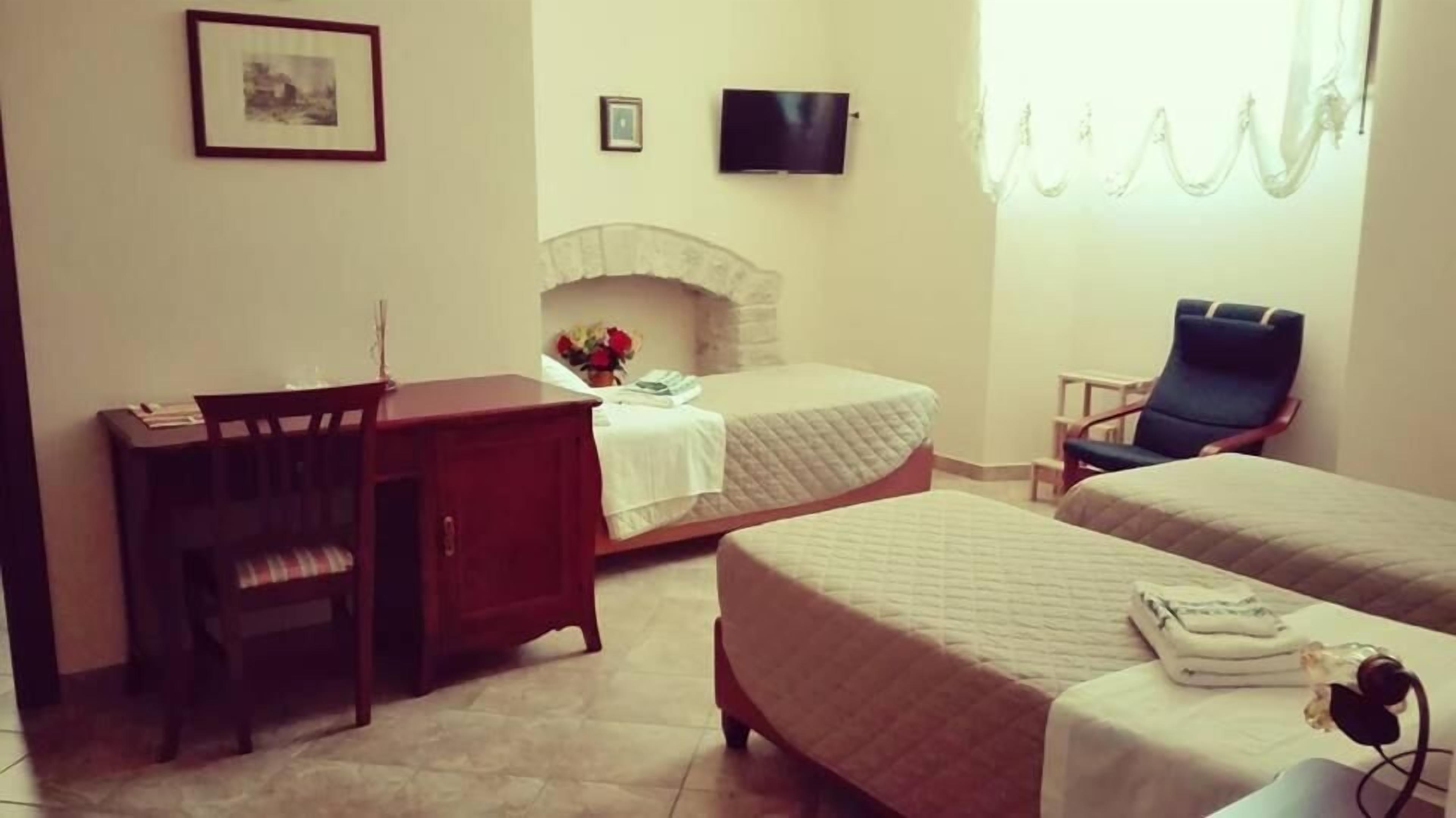 A hotel room with two beds, a desk, a chair, a TV, and a fireplace.