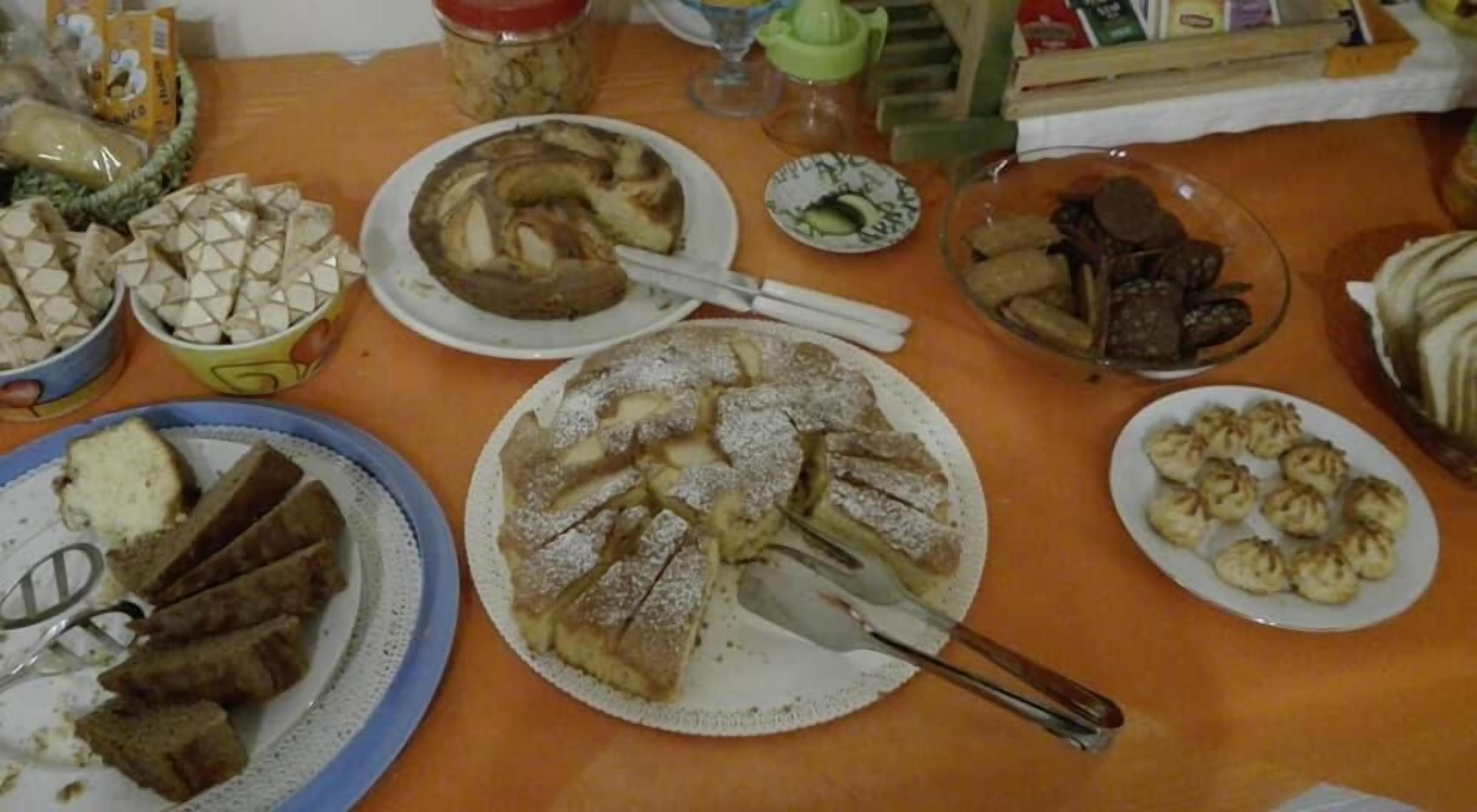 Une table où sont disposés divers plats, notamment un grand gâteau rond, du pain tranché et d’autres aliments.