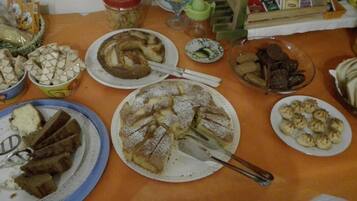 Une table où sont disposés divers plats, notamment un grand gâteau rond, du pain tranché et d’autres aliments.