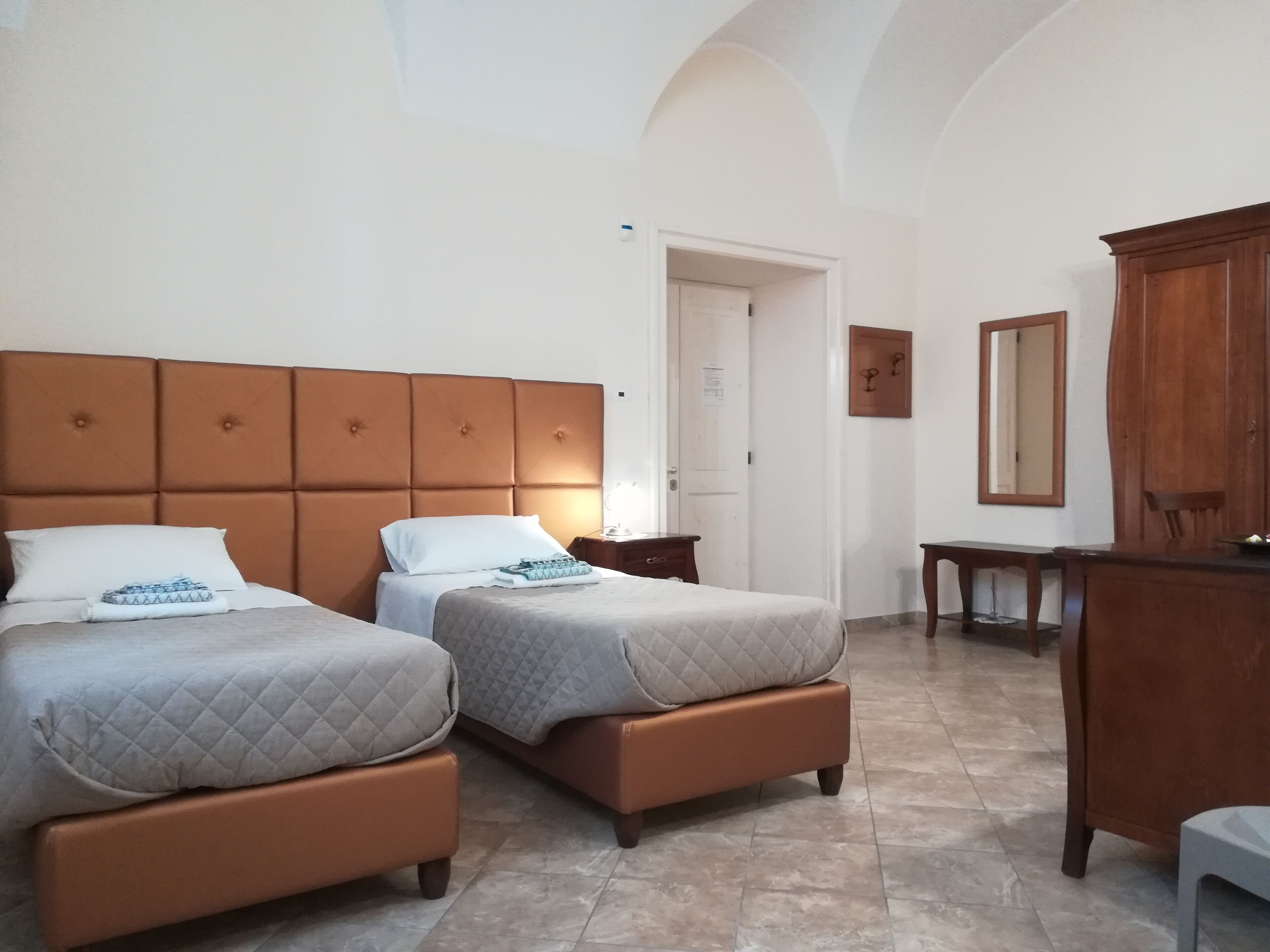 A hotel room with two beds, a wooden wardrobe, a desk, and a mirror.