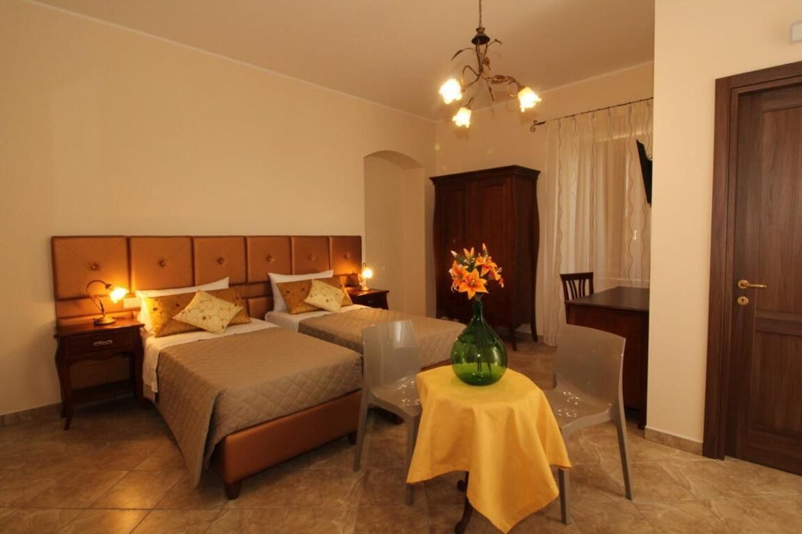 A hotel room with two beds, a dining table with a vase of flowers, a chair, a desk, and a door.