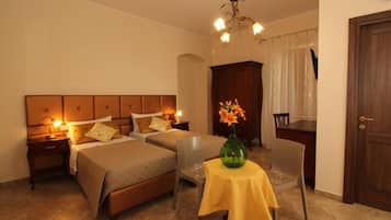 A hotel room with two beds, a dining table with a vase of flowers, a chair, a desk, and a door.