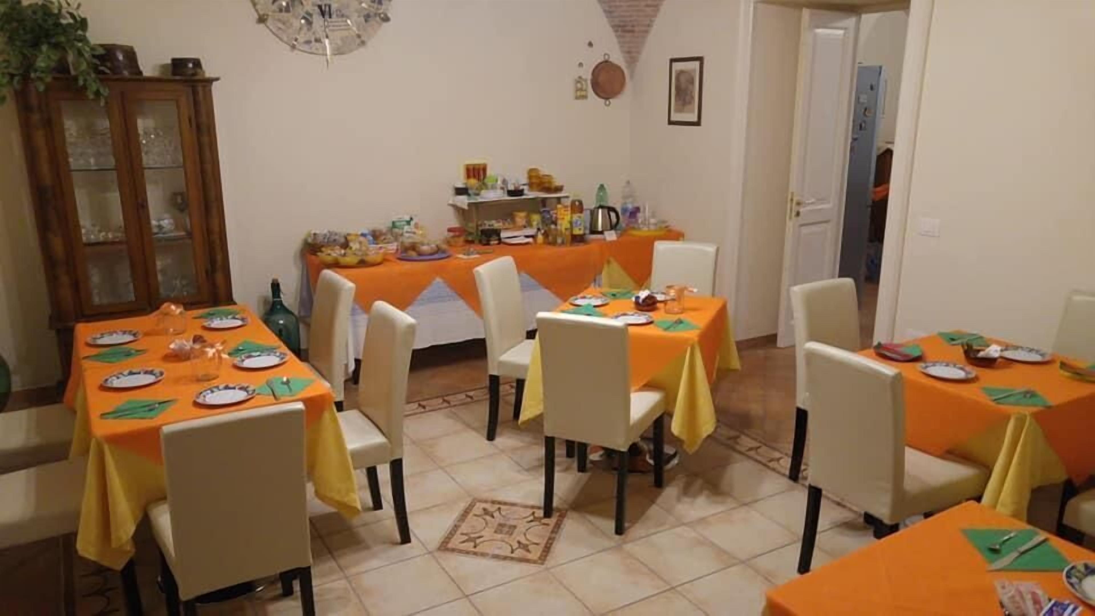 Un espace repas avec plusieurs tables recouvertes de nappes orange, des chaises blanches et un buffet en arrière-plan.