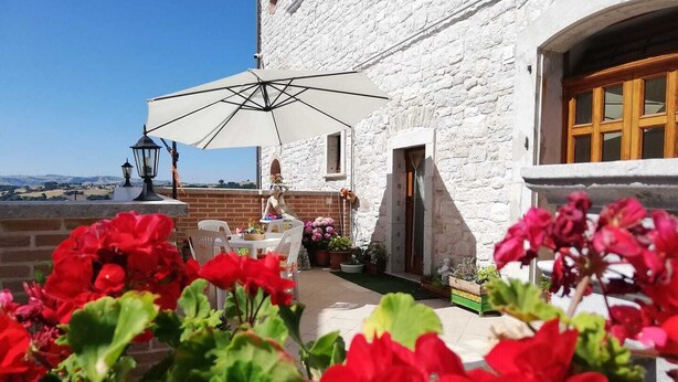 A white building with a stone facade, a wooden door, and a balcony with a table and chairs. - Palazzo 1892 (Castelvetere in Val Fortore)