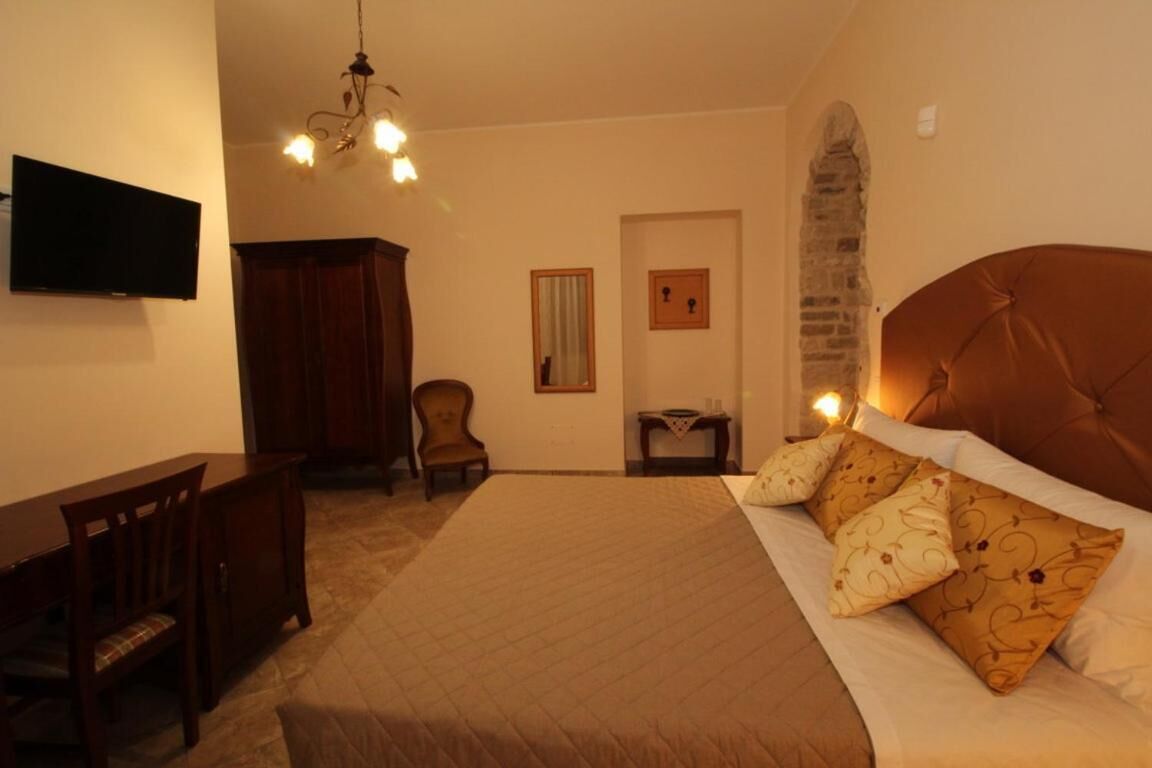 A bedroom with a bed, a desk, a chair, a television, and a chandelier.
