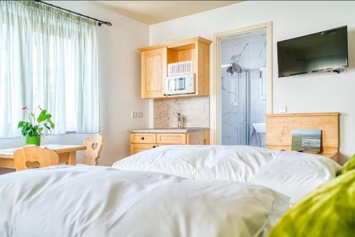A hotel room with two beds, a wooden desk, a microwave, a TV, and a shower.